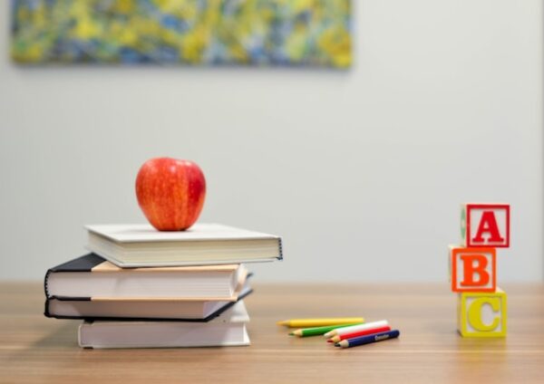 机の上に英語のブロックと色鉛筆と本がつまれており、りんごが本の上に載っている