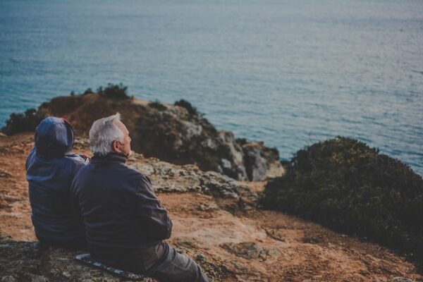 日中、岩の上に座って水域を見つめる 2 人の写真