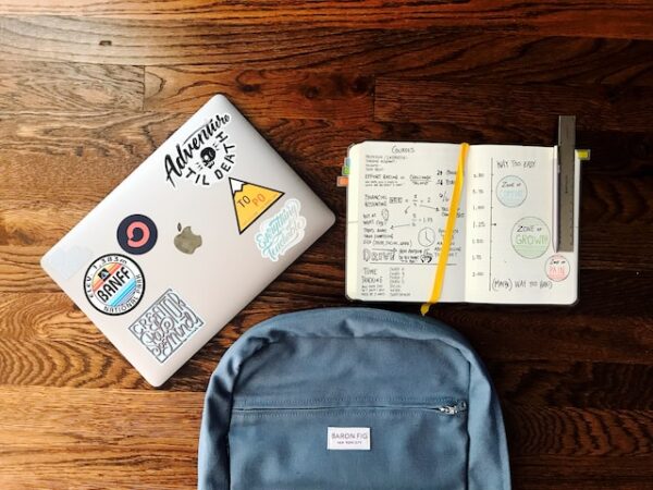 本と銀の MacBook の横にある青いバックパックの平置き写真