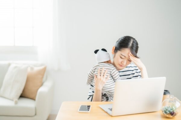 疲れた様子で赤ちゃんを抱いて仕事をする女性