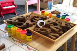 子供用のテーブルにアルファベットの形の木のおもちゃが箱の中に入れられている